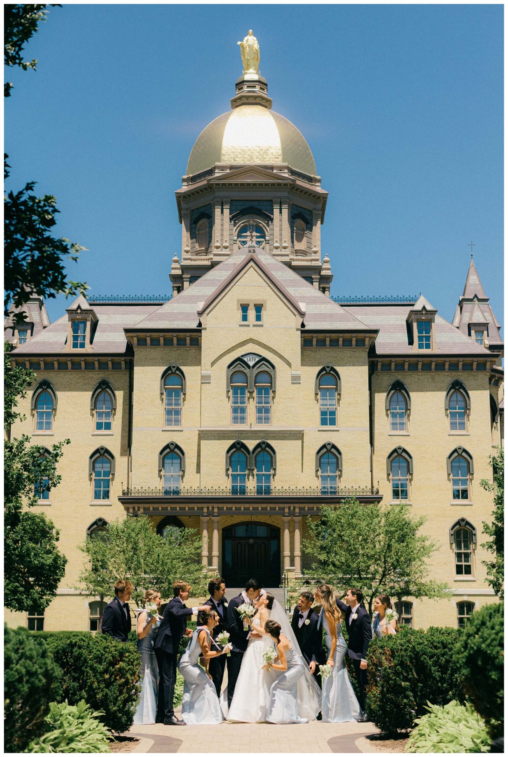 sunny bridal party portrait in front of the main building at Notre dame indiana by josh and andrea photography