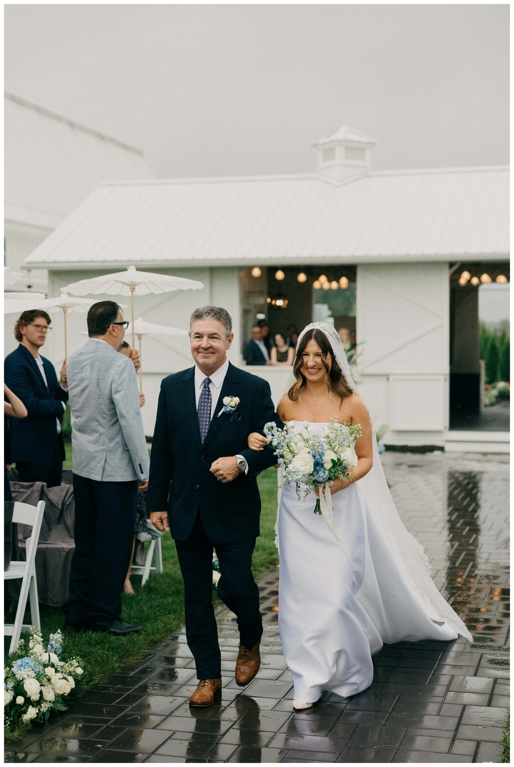 bride walks down aisle in rain at white barn wedding at etre farms by josh and andrea photography 